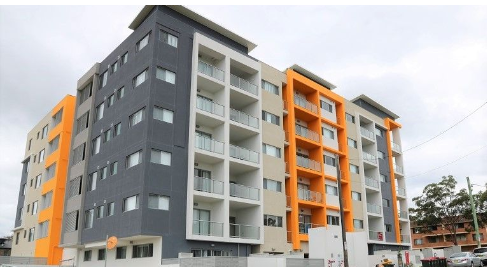 Multistory apartment building with gray, white, and orange exterior walls and balconies, under an overcast sky.